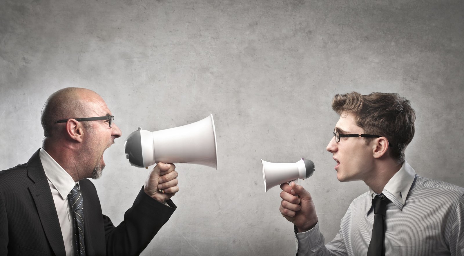 Adult,Businessman,Screaming,Into,A,Megaphone,Against,A,Younger,Businessman